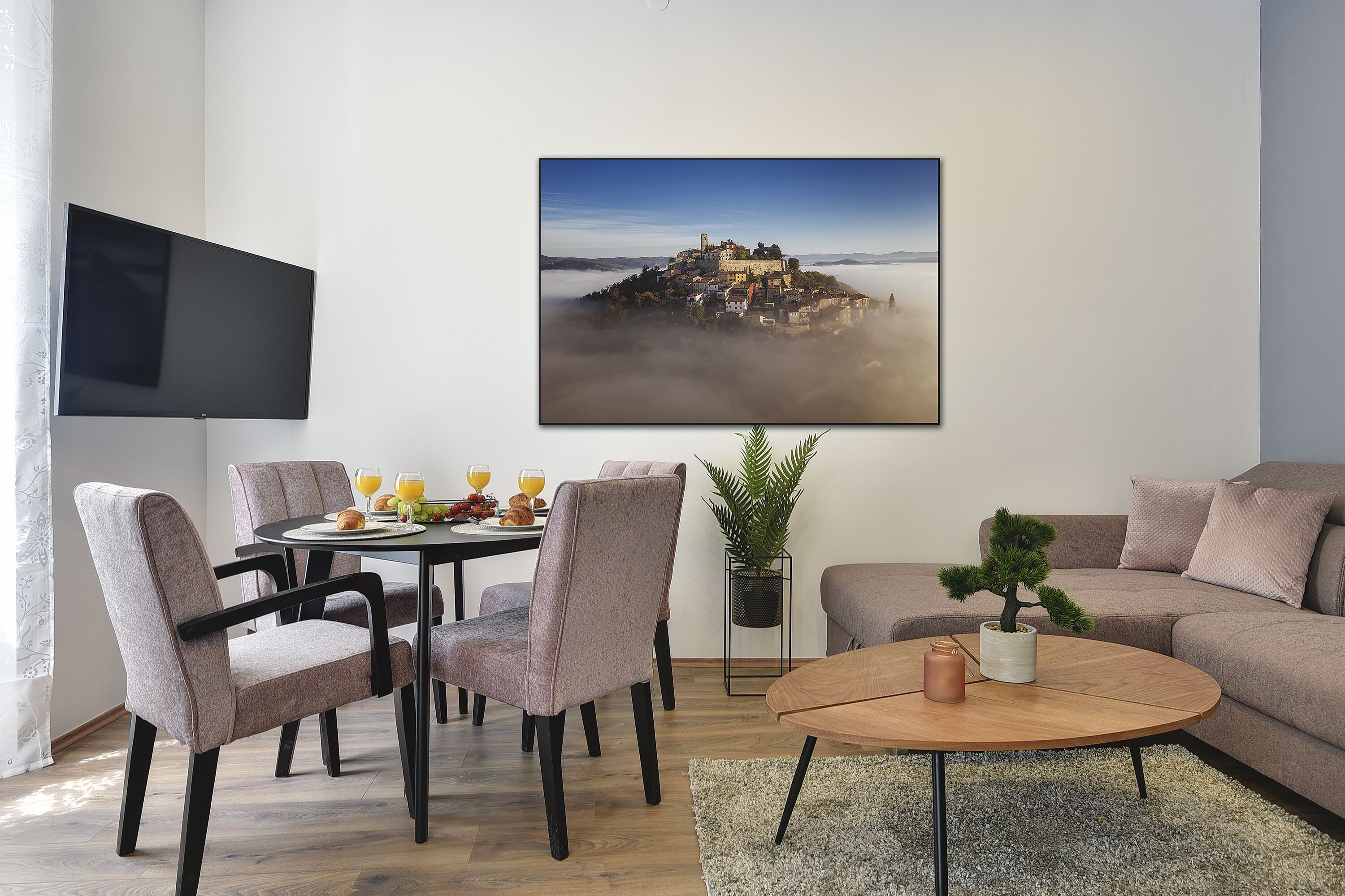A modern living room with a dining area, a flat-screen TV, a large landscape painting, and a cozy seating arrangement.