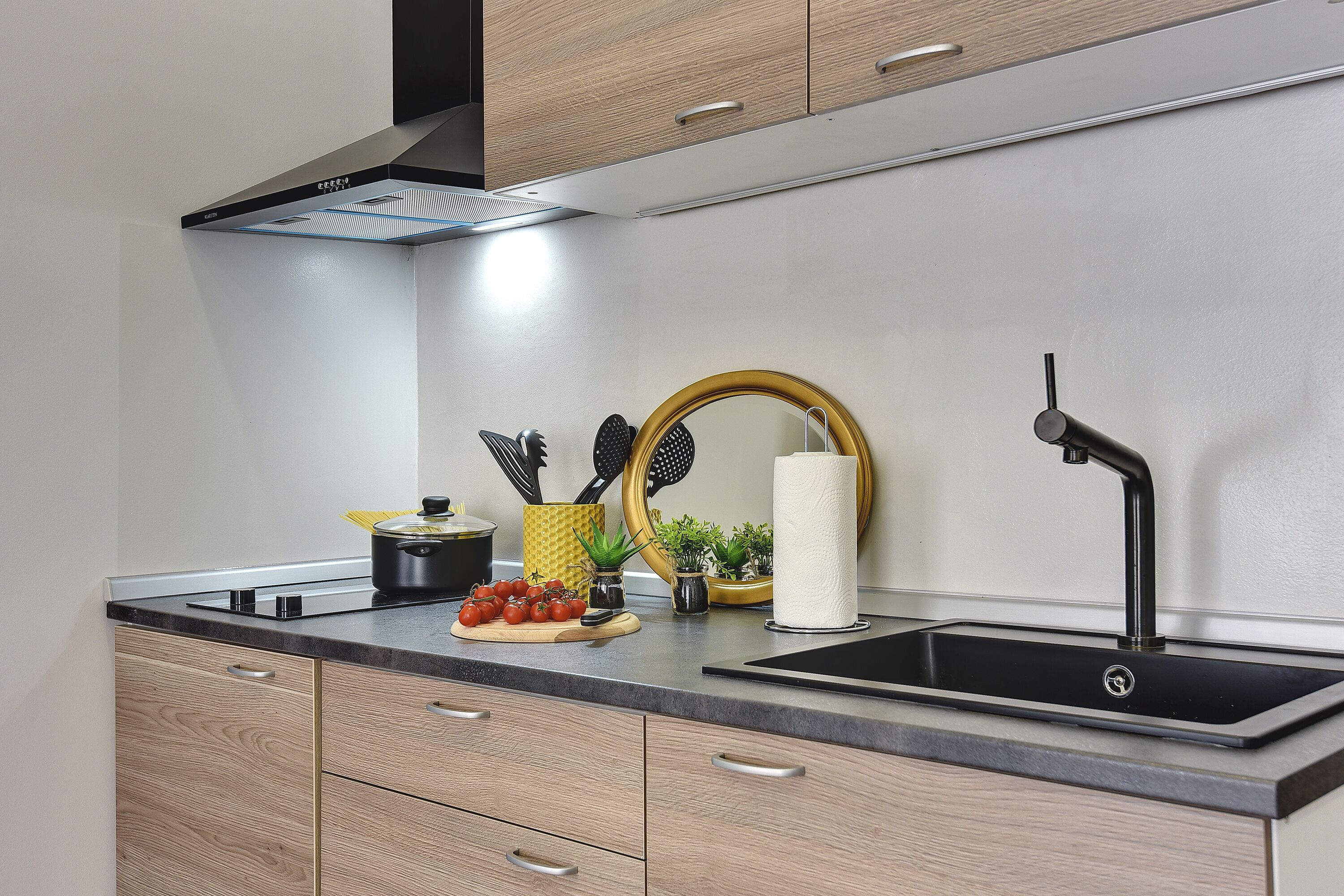 A modern kitchen with wooden cabinets, a black sink, and a stainless steel range hood.