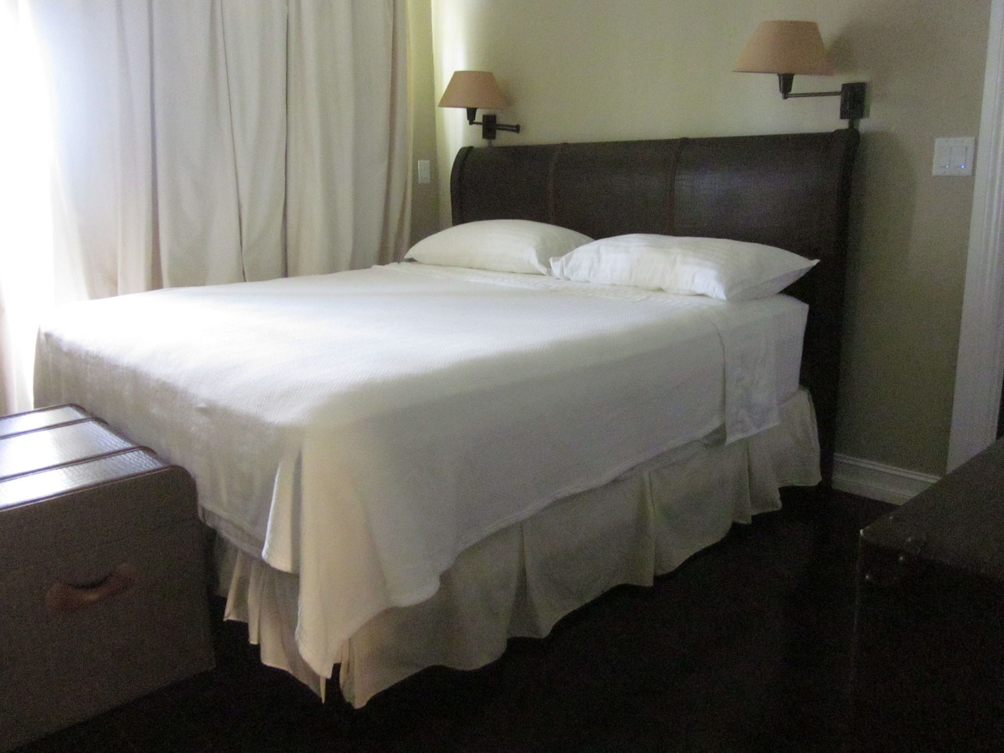 A neatly made bed with white linens, a dark headboard, and two bedside lamps.