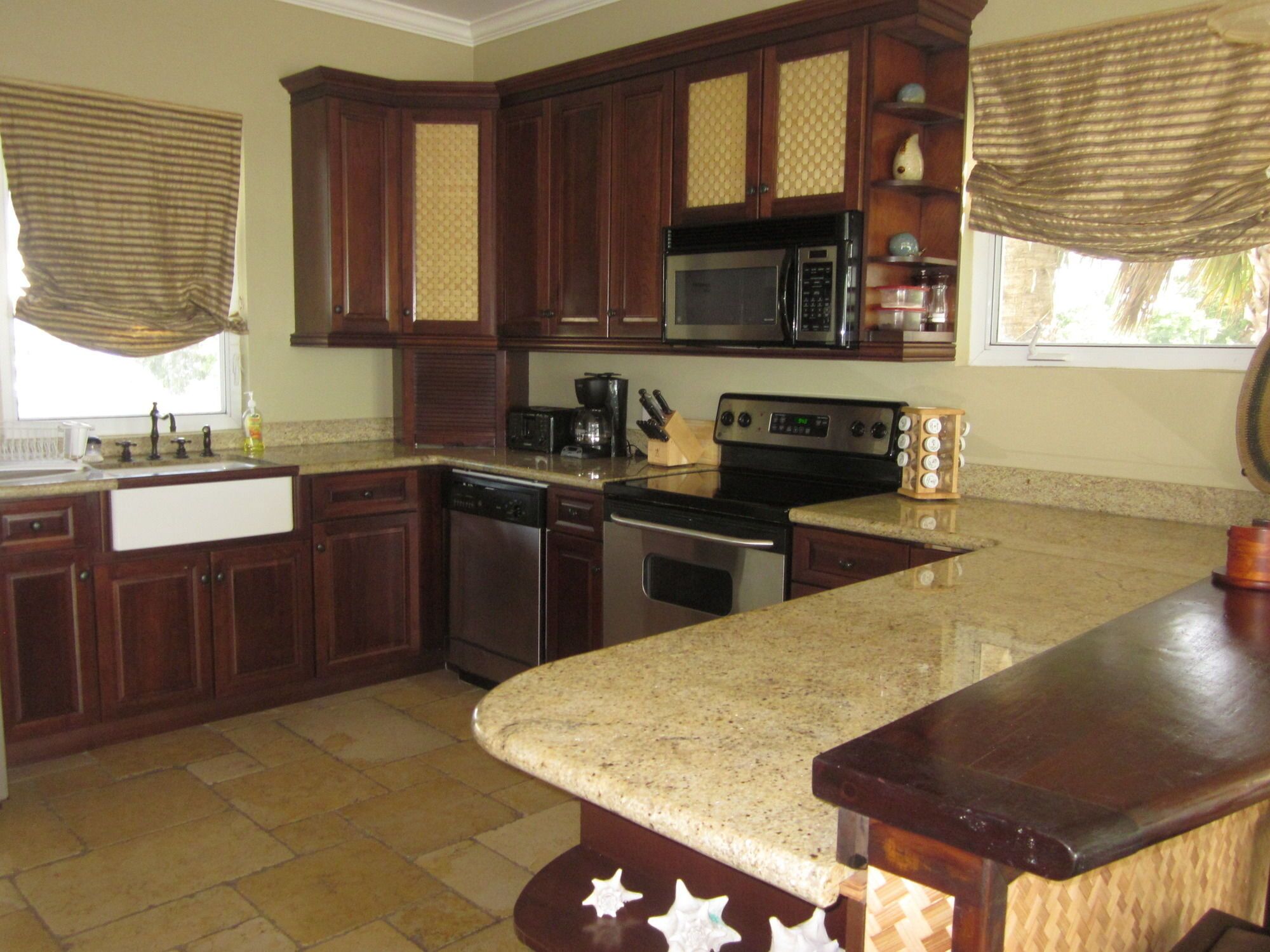 A kitchen with dark wooden cabinets, a granite countertop, stainless steel appliances, and a window with blinds.