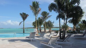 A poolside area with lounge chairs and a 'CAUTION' sign, overlooking a beach and turquoise waters. - February Point Resort Estates BB1 (George Town)