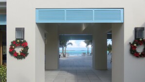 A covered walkway leading to a pool area with palm trees and a view of the ocean. - February Point Resort Estates BB1 (George Town)