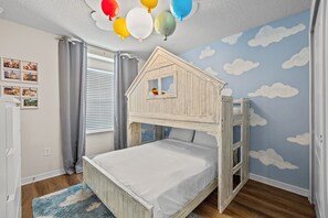A child's bedroom with a bunk bed, a wall mural of clouds, and a ceiling with balloons.