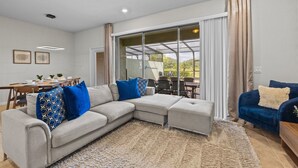 A modern living room with a sectional sofa, a blue armchair, and a dining area with a table and chairs. - 10% off Fall 2026 5-Bedroom Luxury Retreat w/ Modern Updates & Premium Amenities (Davenport)