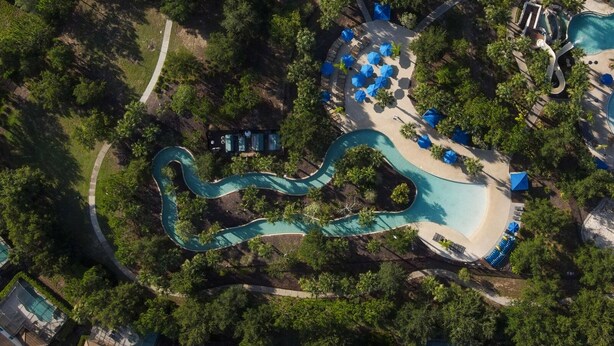 An aerial view of a resort with a winding pool, lounge areas, and dense greenery. - 10% off Fall 2026 5-Bedroom Luxury Retreat w/ Modern Updates & Premium Amenities (Davenport)
