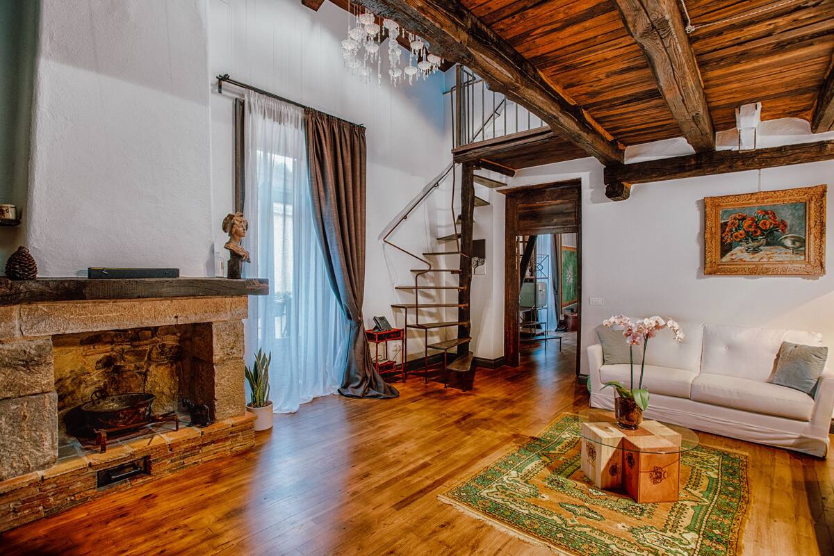 A spacious living room with a fireplace, wooden floors, a white sofa, and a staircase leading to an upper level.