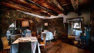 Un'accogliente sala da pranzo rustica, con pareti in pietra, travi in legno e tavoli apparecchiati.