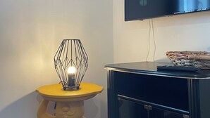 Una habitación con una televisión de pantalla plana montada en la pared, una lámpara decorativa sobre una mesita y un cuadro llamativo encima del televisor.