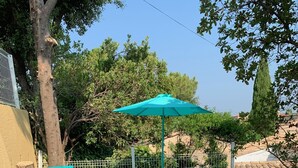 Un patio al aire libre con sillones turquesa y una mesa, rodeado por un muro de piedra y una cerca de metal.