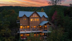 Une grande cabane en bois à plusieurs niveaux, comprenant un balcon et une terrasse, entourée d’une forêt dense.