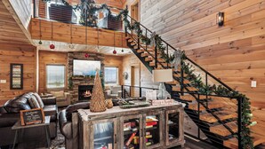 Un intérieur de chalet chaleureux avec un escalier en bois, des sièges en cuir, une cheminée et des décorations de Noël.