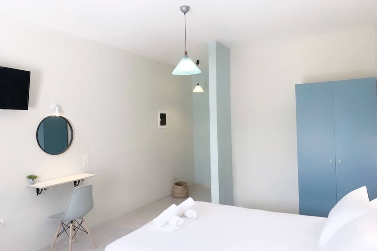 A bedroom with a bed, a desk with a chair, a round mirror, and a blue wardrobe.