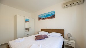 A neatly made bed with pillows, a bedside table with a lamp, a wardrobe, and a painting on the wall. - Spacious room for 8 people near the beach (Seline)