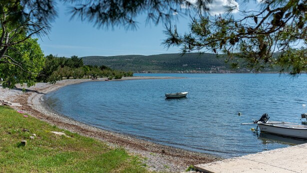 A serene lakeside view with a boat docked on the shore, surrounded by greenery and a clear sky. - Spacious room for 8 people near the beach (Seline)