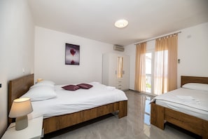 A hotel room with a wooden bed, a nightstand with a lamp, a wardrobe, and a sliding glass door to the balcony.