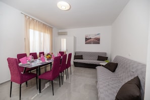 A dining area with a table set for six, surrounded by pink chairs, and a grey sofa in the living area.