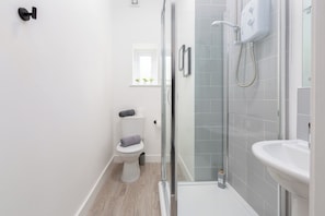 A modern bathroom with a glass shower enclosure, a white sink, and a toilet. - Charnley House Apartment 3 (Blackpool)