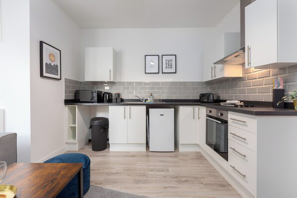 A modern kitchen with white cabinets, a black refrigerator, a microwave, and a coffee machine.