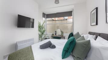 Habitació d'hotel moderna amb un llit, una televisió plana penjada a la paret, un escriptori amb una cadira i un gran finestral que ofereix vistes a la ciutat.