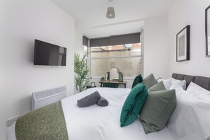 Ein modernes Hotelzimmer mit Bett, Flachbildfernseher an der Wand, Schreibtisch mit Stuhl und großem Fenster mit Blick auf die Stadt.