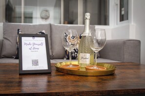 A framed welcome sign with a QR code on a wooden table, a bottle of Freixenet Prosecco, and two wine glasses on a gold tray.