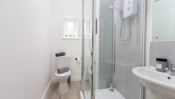 Un bany modern amb una cabina de dutxa de vidre, un lavabo blanc i un vàter.