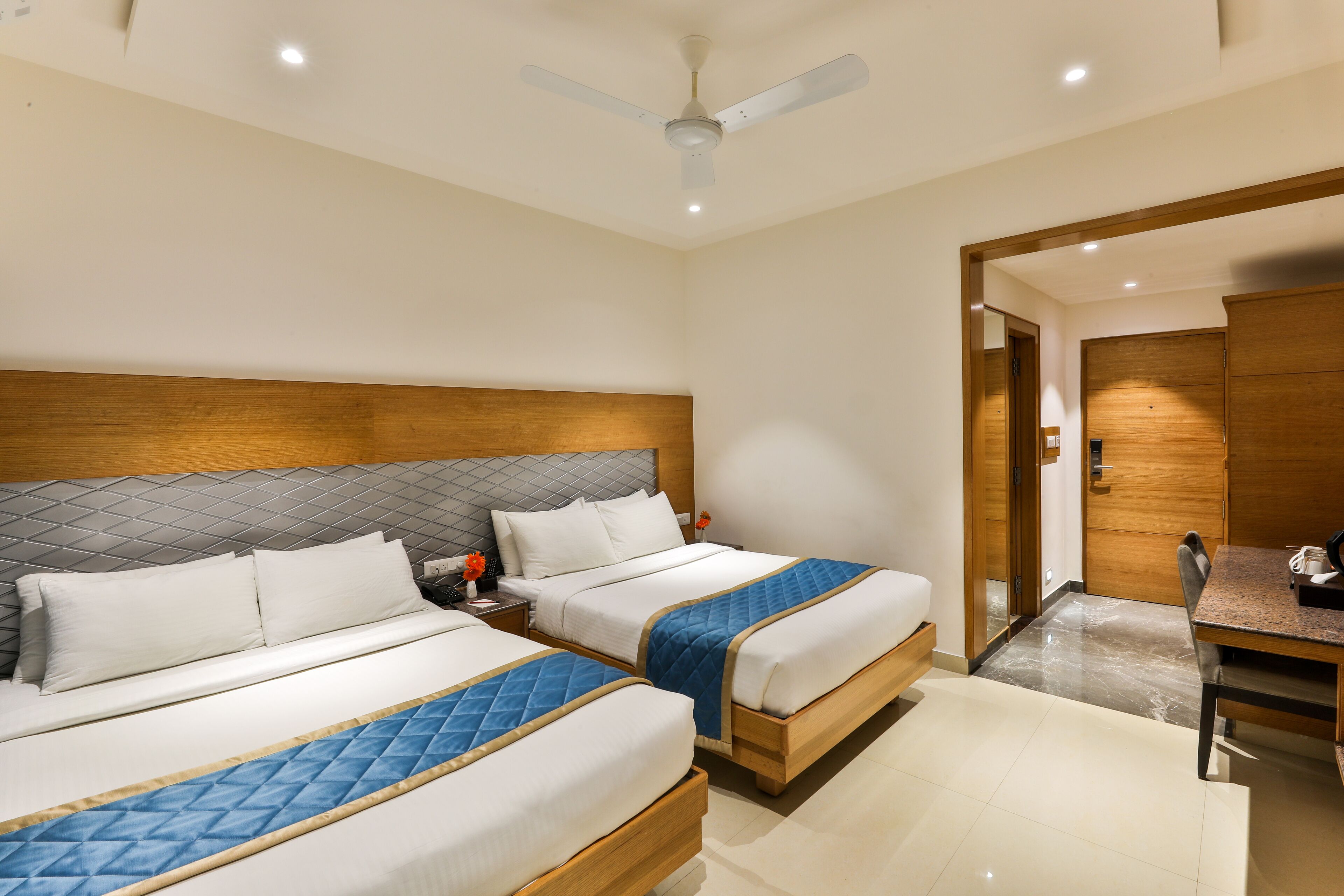 Habitación de hotel con dos camas, cabecero de madera, escritorio y ventilador de techo.