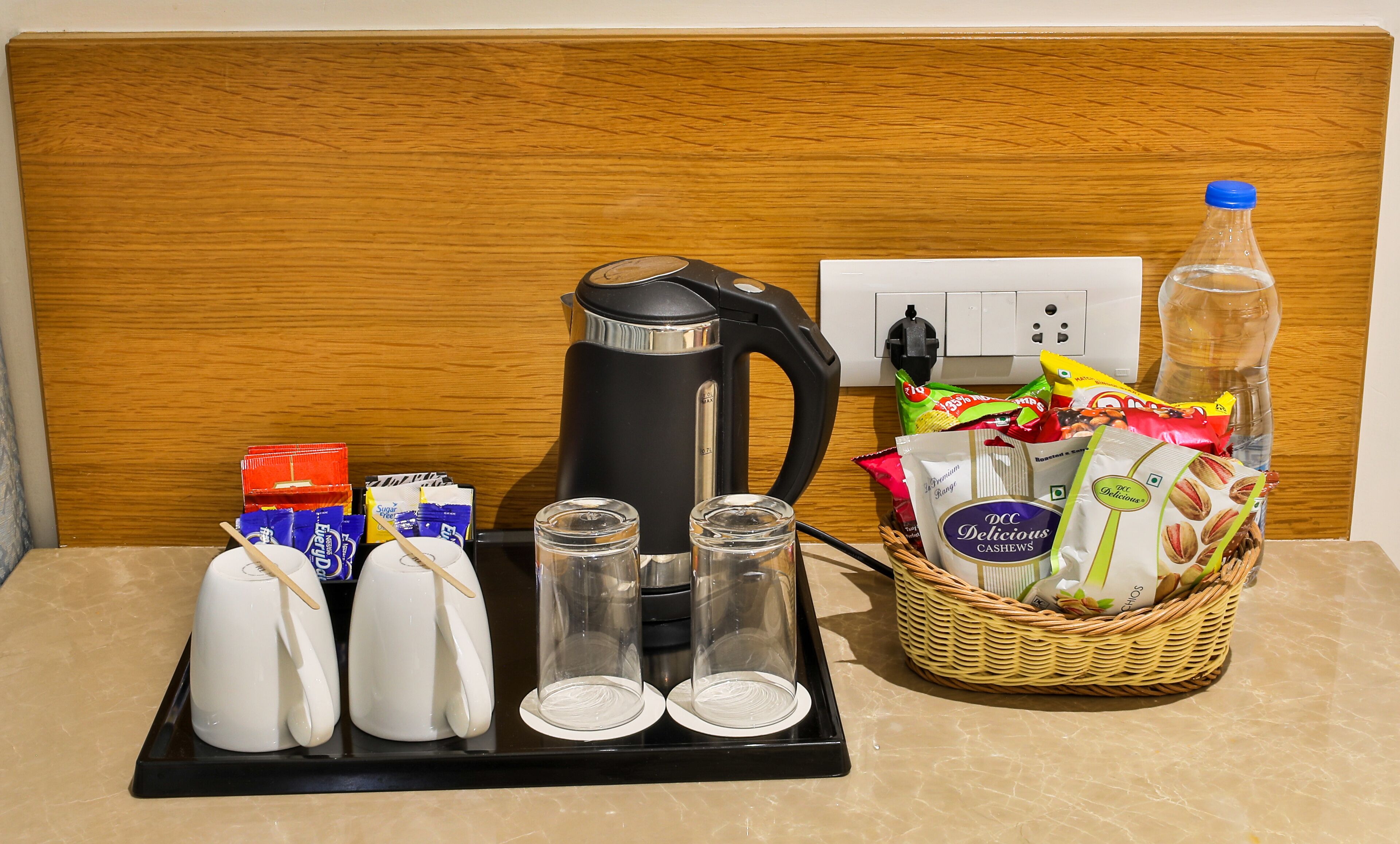 A breakfast setup with a kettle, teapots, glasses, and a basket of snacks.