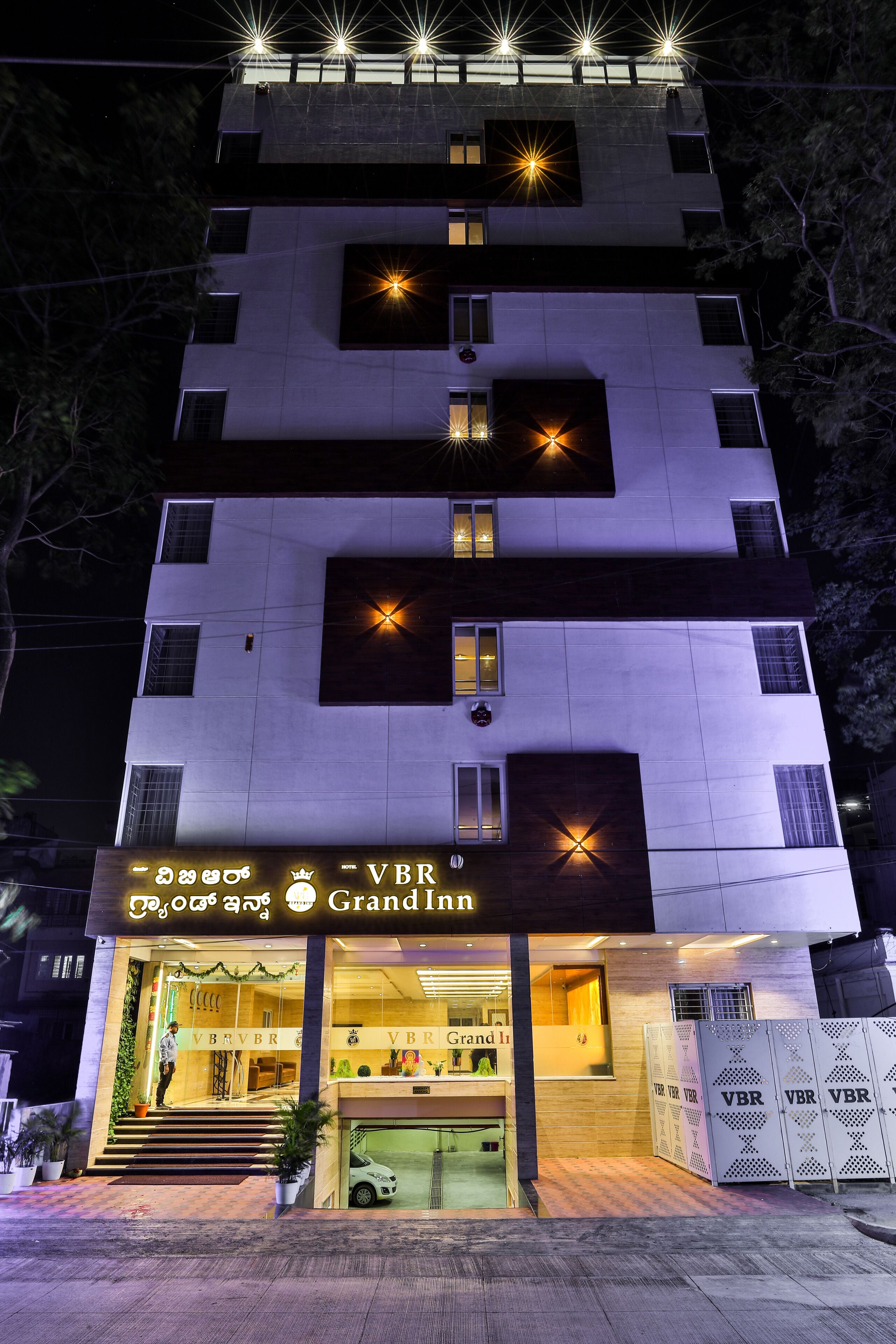 Un hotel urbà de diversos pisos amb un disseny modern, que destaca per una entrada prominent amb un rètol que diu "VBR Grand Inn".
