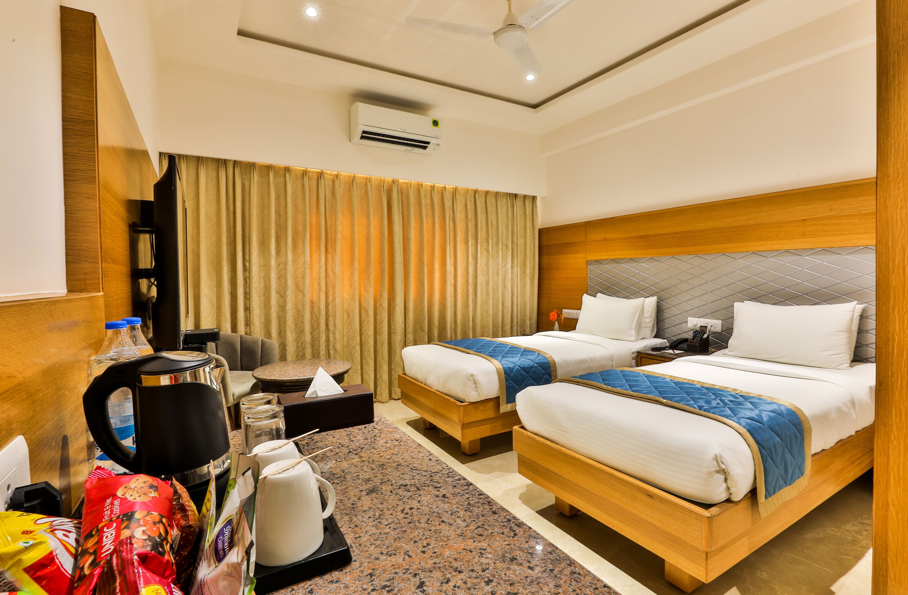 A hotel room with two beds, a coffee maker, a kettle, a minibar, and an air conditioning unit.