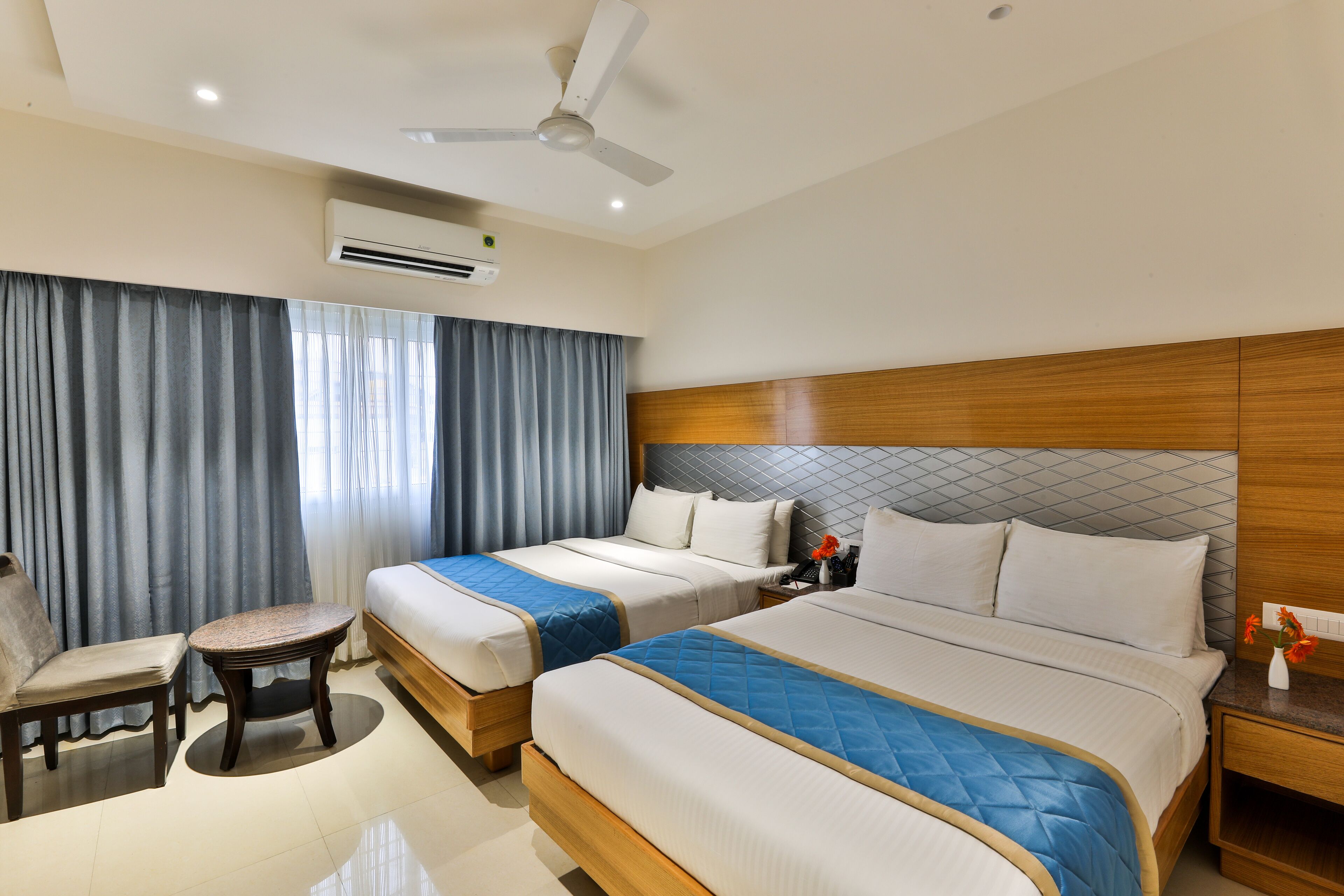 A hotel room with two beds, a chair, a nightstand, and a ceiling fan.