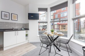 A modern kitchen with white cabinetry, a black countertop, and a dining area with a table set for four.