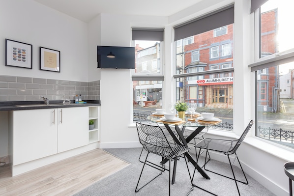 A modern kitchen with white cabinetry, a black countertop, and a dining area with a table set for four.