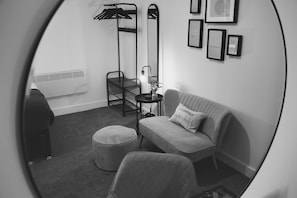 A compact room with a sofa, a chair, a small table with a lamp, a mirror, and a radiator.
