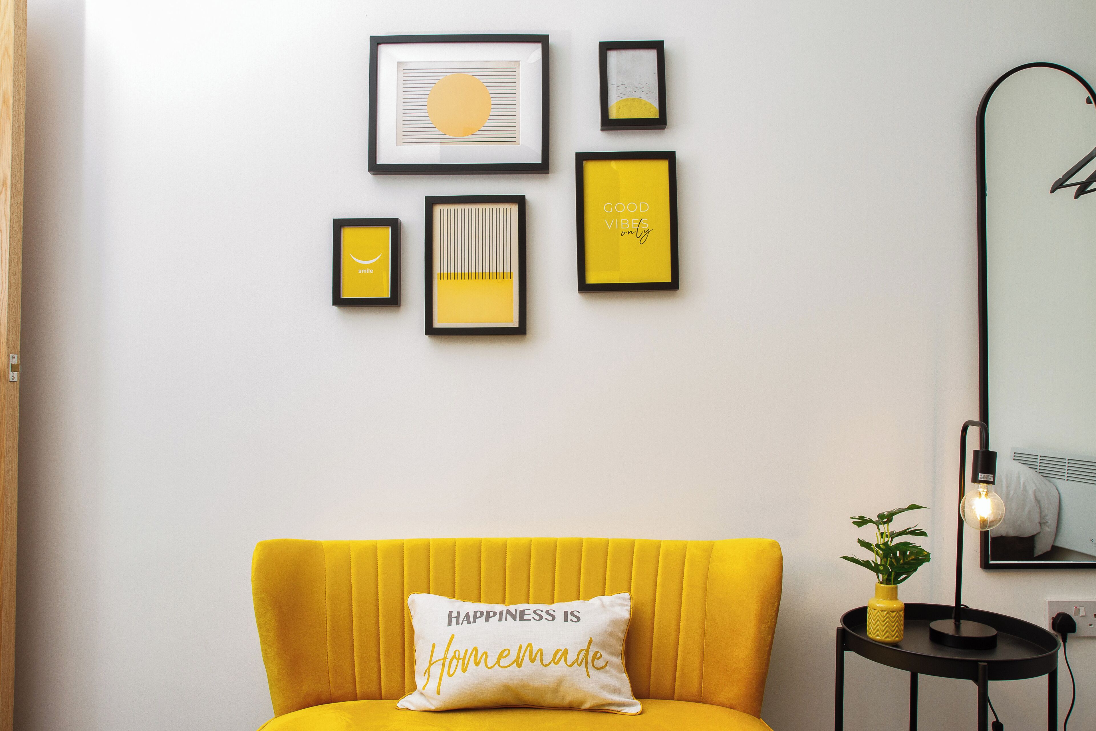 A room with a yellow sofa, a wall with framed artwork, and a mirror.