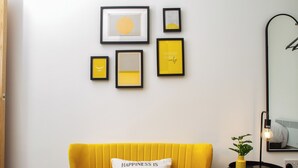 Una stanza con un divano giallo, una parete decorata con opere d'arte e uno specchio.