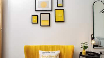 A room with a yellow sofa, a wall with framed artwork, and a mirror.