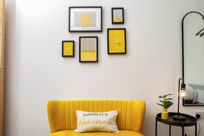 A room with a yellow sofa, a wall with framed artwork, and a mirror.