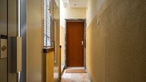 A narrow hallway with a wooden door at the end, a doormat, and a light switch on the wall. - Apartment (Lisboa)