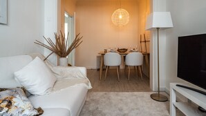 A modern living room with a sofa, a TV, a dining area with chairs, and a pendant light. - Apartment (Lisboa)