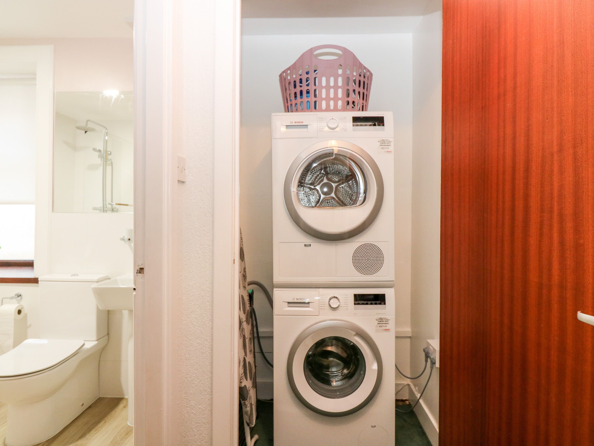 Un área de lavandería con dos lavadoras apiladas y una secadora, una ducha y un inodoro.