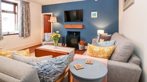 A living room with a fireplace, a television mounted on the wall, and a sofa with patterned cushions. - 4 Gordon Street (Buckie)