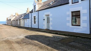 A row of white buildings with dark roofs, a clear sky, and a road in the foreground. - 4 Gordon Street (Buckie)