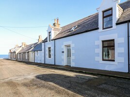 A row of white buildings with dark roofs, a clear sky, and a road in the foreground.