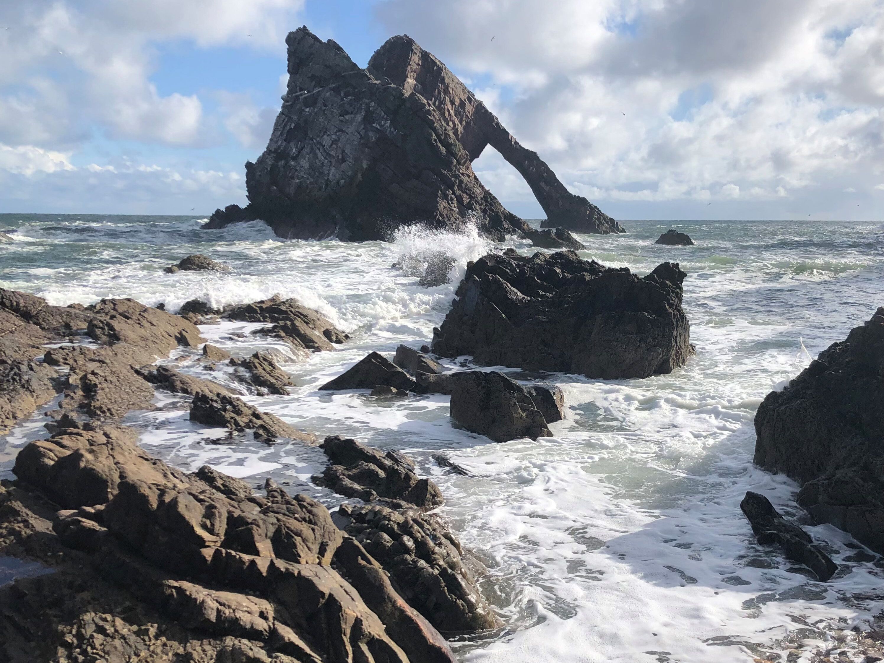 A rocky coastline with large boulders and a prominent rock formation arching over the water.