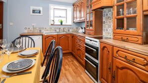 A kitchen with wooden cabinets, a built-in oven, and a dining area with a table set for four. - 4 Gordon Street (Buckie)