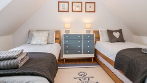 A cozy attic bedroom with two beds, a dresser, and a wall-mounted shelf with framed pictures. - 4 Gordon Street (Buckie)