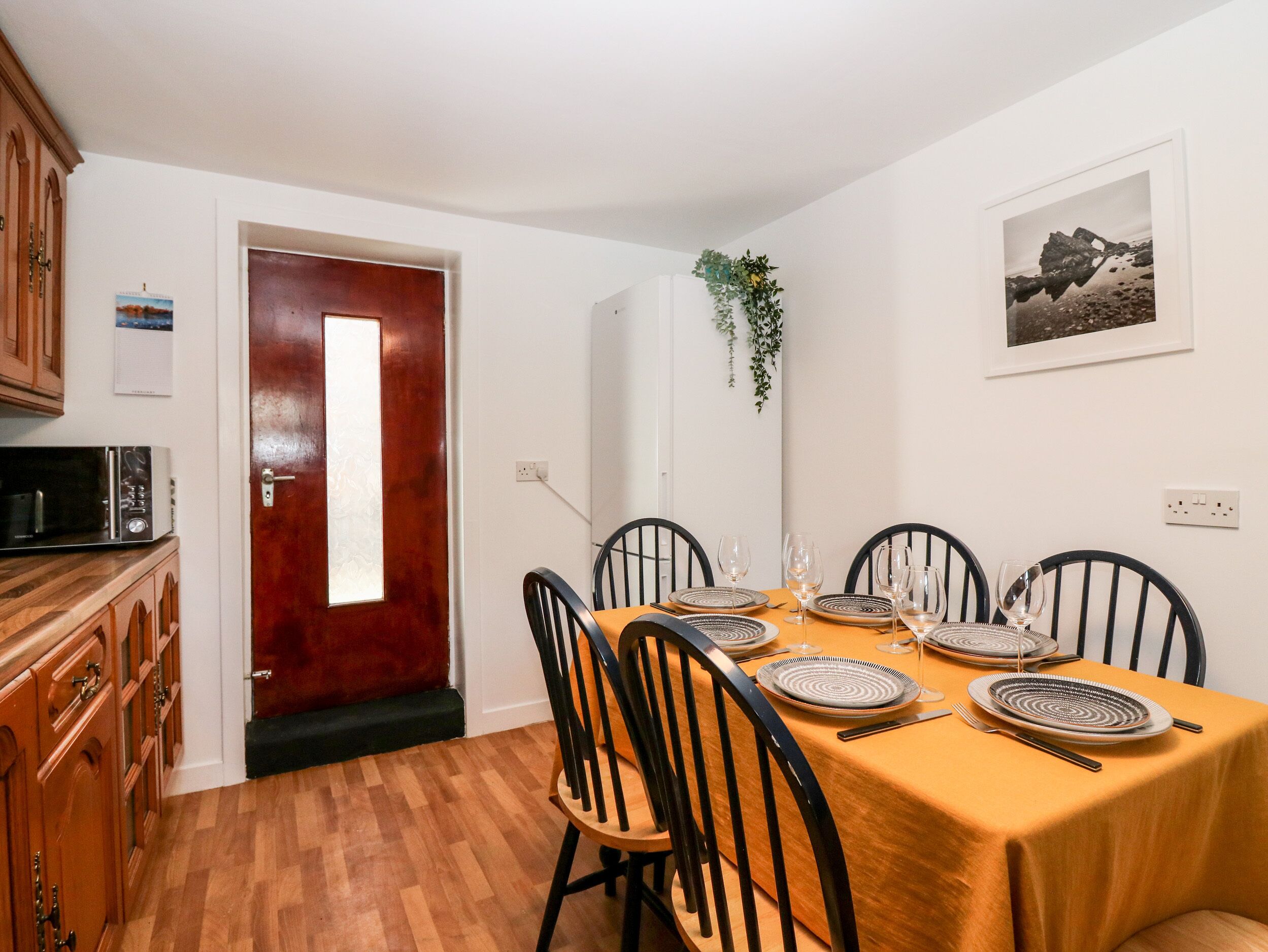 A dining area with a wooden table set for four, black chairs, and a red door.