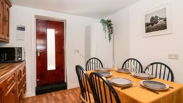 A dining area with a wooden table set for four, black chairs, and a red door.