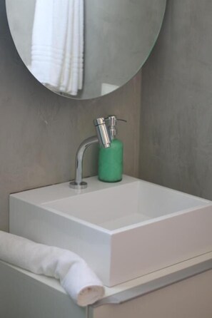 Ein Badezimmer mit einem weißen Waschbecken, einem runden Spiegel und einer grünen Seifenspender.